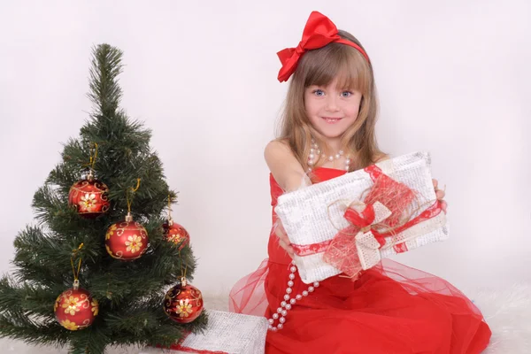 Emocionální portrét veselá dívka v červených šatech. Novoroční dárek pod stromeček — Stock fotografie