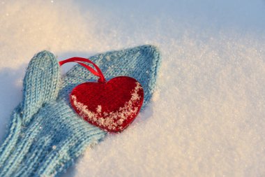 Beyaz kar üzerinde gri örülmüş bir eldivenin üzerindeki kırmızı bir kalp. Boşluğu kopyala.