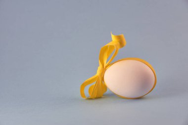 Sarı kurdeleli beyaz tavuk yumurtası ve yumuşak mavi bir arka plan. Paskalya konsepti.