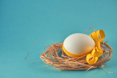 Turkuaz arka planda turuncu kurdeleli bir yuvada beyaz bir yumurta. Paskalya konsepti.