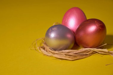 Sarı arka planda, yuvadaki inci renkli yumurtalar. Paskalya konsepti.