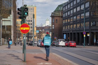 HELSINKI, FINLAND - 30 Nisan 2021: Yiyecek getiren çantalı genç bir adam Wolt sokakta scooter sürüyor.