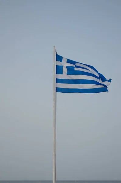 Le drapeau de la Grèce est hissé sur le mât du drapeau contre le ciel bleu. — Photo