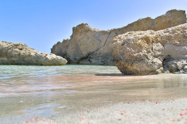 Sziklák a homokos tengerparton kék vízzel és rózsaszín homokkal. — Stock Fotó