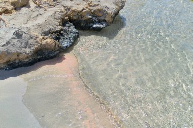 Kumlu pembe kumsal kayalık taşlar ve deniz suyuyla.
