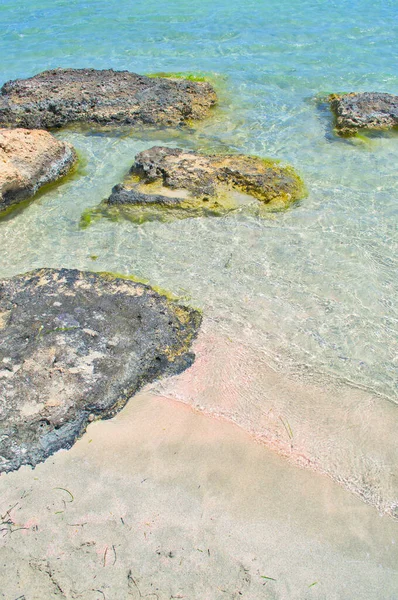 Песчаный розовый пляж с каменистыми камнями и лазурной морской водой. — стоковое фото