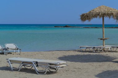 Güneş pansiyonları ve deniz kıyısında bir kamış plaj şemsiyesi.