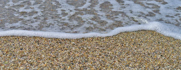 Die Textur des weißen Randes der Meereswelle und der verschwommene Sand im Vordergrund. — Stockfoto