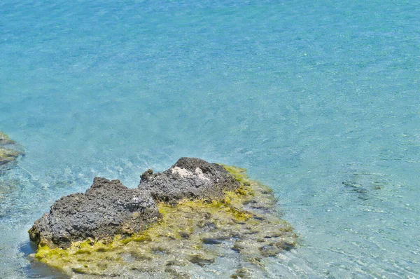 Rotsachtige steen aan de azuurblauwe kust van de zee. — Stockfoto