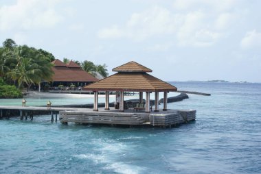 Okyanustaki çardak, tatil köyüne ahşap köprüyle bağlı. Uzak yapı, tropikal ağaçlarla çevrili Maldivler 'deki Kurumba Adası tatil beldesi. Hint Okyanusu 'nun sakin ve güzel mavi tonları ufuk yanılsaması yaratır..!