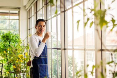 Asyalı adam kahve tutuyor ve pencerenin yanında duruyor kahve molası zamanı