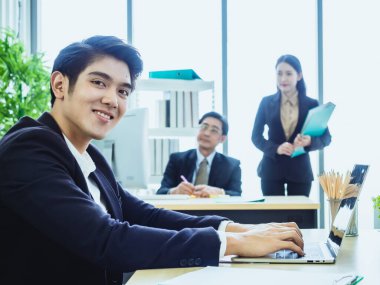 Genç Asyalı iş adamı. Gülümse. oturarak ve ofiste durarak. İş konuşalım. Resmi çalışma geçmişi olan bir telefon görüşmesi. kamera çapraz kol kopyalama alanı