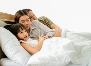 Mutlu aile yatak odası konseptinde eğleniyor. Baba, anne ve kız gülen surat, aşk öpücüğü birlikte yatakta yorganla yatıyorlar kopya alanlarını kaplıyorlar..