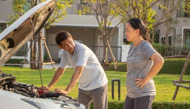 Bozuk araba cep telefonundan yardım istiyor. Yoldaki bozuk araba. Asyalı bir adam ve kadın kırık bir arabanın yakınındalar..