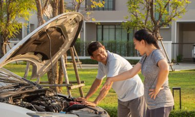 Bozuk araba cep telefonundan yardım istiyor. Yoldaki bozuk araba. Asyalı bir adam ve kadın kırık bir arabanın yakınındalar..
