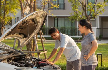 Bozuk araba cep telefonundan yardım istiyor. Yoldaki bozuk araba. Asyalı bir adam ve kadın kırık bir arabanın yakınındalar..
