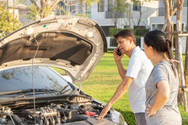 Bozuk araba cep telefonundan yardım istiyor. Yoldaki bozuk araba. Asyalı bir adam ve kadın kırık bir arabanın yakınındalar..