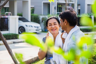Birkaç yaşlı Asyalı erkek ve kadın sabah egzersizlerinden önce egzersiz kıyafeti giyerler. Yaşlı erkekler ve kadınlar bahçede koştuktan sonra terlerini silmek için havlu kullanırlar.