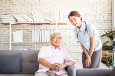 Huzurevi konseptinde kıdemli adam. Hemşire, huzurevinde oturma odasında yaşlı bir adamla oturuyor. Kameraya bakıyor ve gülümsüyor.