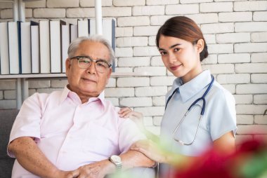 Huzurevi konseptinde kıdemli adam. Hemşire, huzurevinde oturma odasında yaşlı bir adamla oturuyor. Kameraya bakıyor ve gülümsüyor.