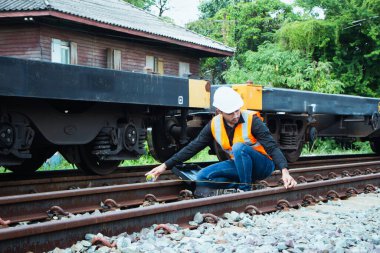 Başlık ve yelek giyen Müfettiş Mühendislik demiryolu inşaatını kontrol etmekten aranıyor. Asyalı işçiler demiryolu raylarını ölçmek için mezura kullanıyor.