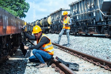 Başlık ve yelek giyen Müfettiş Mühendislik demiryolu inşaatını kontrol etmekten aranıyor. Asyalı işçiler koordine etmek için telsiz kullanıyor..