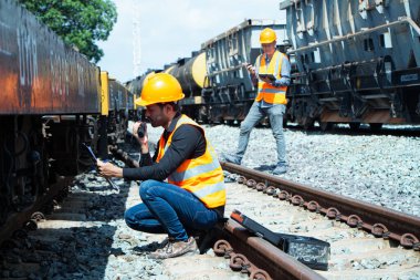 Başlık ve yelek giyen Müfettiş Mühendislik demiryolu inşaatını kontrol etmekten aranıyor. Asyalı işçiler koordine etmek için telsiz kullanıyor..
