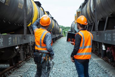 Başlık ve yelek giyen Müfettiş Mühendislik demiryolu inşaatını kontrol etmekten aranıyor. Bir ortağa danışmanlık yapan Asyalı bir işçi.