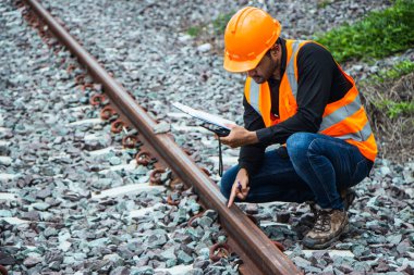 Başlık ve yelek giyen Müfettiş Mühendislik demiryolu inşaatını kontrol etmekten aranıyor. Asyalı işçiler ve iş arkadaşları eski tren araçlarının yanında dururlar..