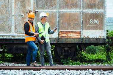 Başlık ve yelek giyen Müfettiş Mühendislik demiryolu inşaatını kontrol etmekten aranıyor. Asyalı işçiler ve iş arkadaşları eski tren araçlarının yanında dururlar..
