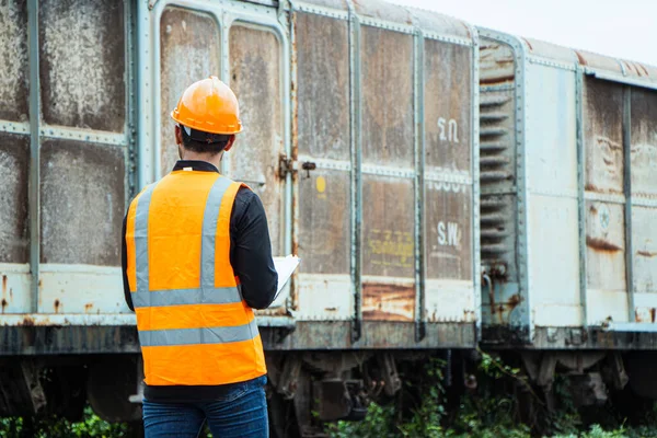 Inspector Engineering wearing helmet and vest worker unifrom checking railway construction work on rail track. Asian workers and coworkers stand beside old train bogies.