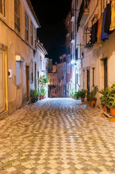 Portekiz 'in başkenti Lizbon' daki turist Alfama 'nın parke taşı zeminiyle süslenmiş dar bir caddenin gece manzarası.