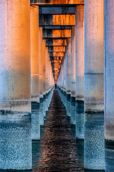 Sunset between columns that form the base of a bridge on the sea — Stock fotografie