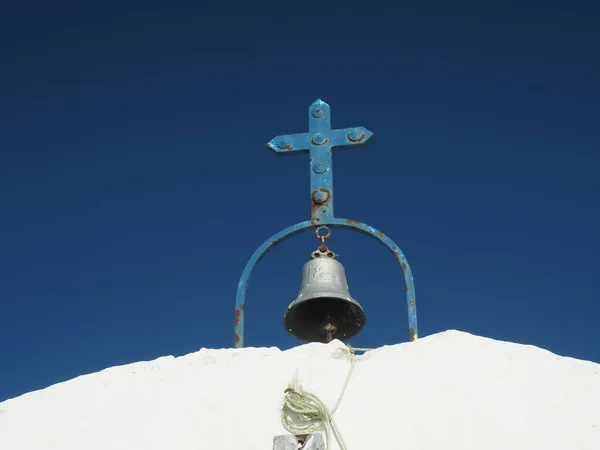 Paslı eski mavi metal haç ve çan, açık mavi arka planlı, küçük, beyaz, geleneksel bir Yunan Ortodoks kilisesinin tepesinde.