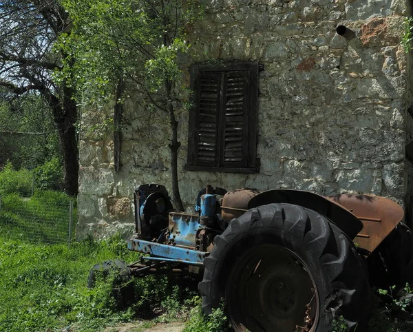 Yunanistan 'ın Atina kenti yakınlarındaki Tatoi parkındaki terk edilmiş taş çiftlik binasının dışındaki paslı eski traktör manzarası.