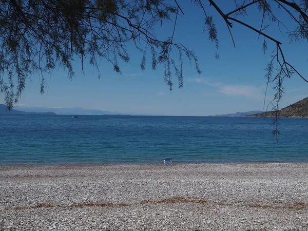 Yunanistan 'ın Psatha kentinde, açık mavi gökyüzü ve açık denizle ıssız bir plajda su kenarındaki tek sandalyenin görüntüsü