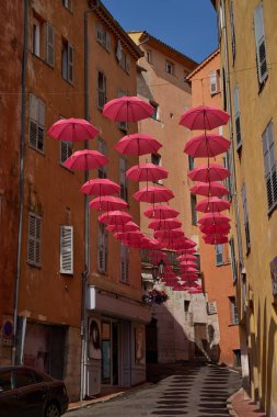 Grasse, Fransa - 12 Haziran 2025 - Pembe şemsiyeli bir Avrupa kasabasında büyüleyici bir ara sokak                               