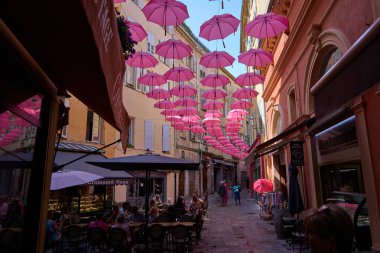 Grasse, Fransa - 12 Haziran 2025 - Pembe şemsiyeli bir Avrupa kasabasında büyüleyici bir ara sokak                               