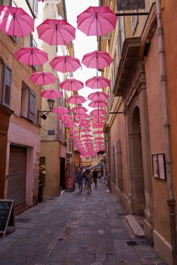 Grasse, Fransa - 12 Haziran 2025 - Pembe şemsiyeli bir Avrupa kasabasında büyüleyici bir ara sokak                               