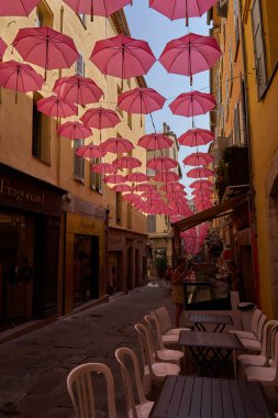 Grasse, Fransa - 12 Haziran 2025 - Pembe şemsiyeli bir Avrupa kasabasında büyüleyici bir ara sokak                               