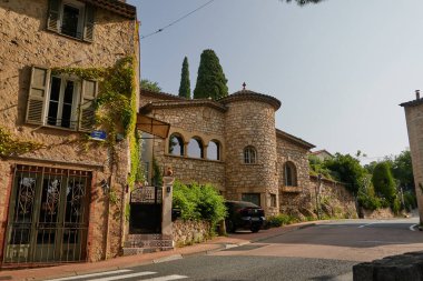 Valbonne, Fransa - 13 Haziran 2025 - Sarmaşıklı ve sessiz bir caddeye park edilmiş siyah arabalı hoş bir taş bina                               