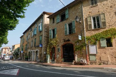 Valbonne, Fransa - 13 Haziran 2025 - Sarmaşıklı ve sessiz bir caddeye park edilmiş siyah arabalı hoş bir taş bina                               