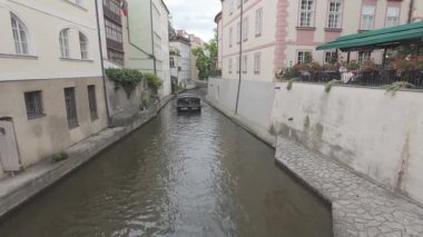 Prag, Çek Cumhuriyeti - 5 Temmuz 2024 - Tur teknesi Avrupa 'nın tarihi binaları ve açık kafe koltukları arasında dar bir kanalda ilerliyor
