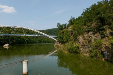 Brno, Çek Cumhuriyeti - 16 Ağustos 2025 - Brno Barajı - Modern kemer köprüsü, mavi gökyüzü altındaki yemyeşil ormanlarla çevrili