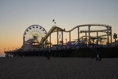 Los Angeles, ABD - 18 Ekim 2025 - Santa Monica İskelesi Gün batımında Sahilden ve lunaparktan keyif alan insanların siluetleriyle