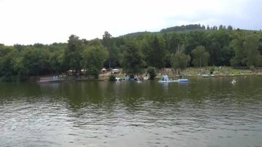 Brno, Çek Cumhuriyeti - 16 Ağustos 2025 - Brno Barajı - İnsanlar şişme su oyuncakları ve ağaçlarla dolu kalabalık bir barajda güneşli bir günün tadını çıkarıyorlar