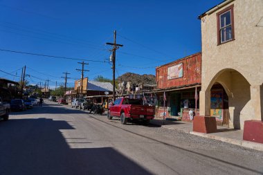 Oatman, Arizona, ABD - 19 Ekim 2025 - Güneşli bir günde antika dükkanları, park edilmiş araçları ve motosikleti olan eski batı kasabası caddesi