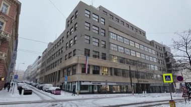 Prag, Çek Cumhuriyeti - 12 Ocak 2026 - Çek Radyo Binası. Yol boyunca park etmiş modern mimarisi ve arabaları olan karlı şehir caddesi.