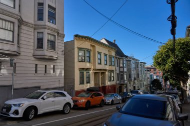 San Francisco, ABD - 28 Ekim 2025 - San Francisco Viktorya dönemi mimarisi dik bir tepede park etmiş arabalarla ve açık mavi gökyüzüyle