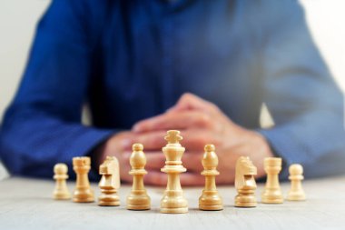 Satranç taşlarının önünde elleri bağlı oturan bir iş adamı.